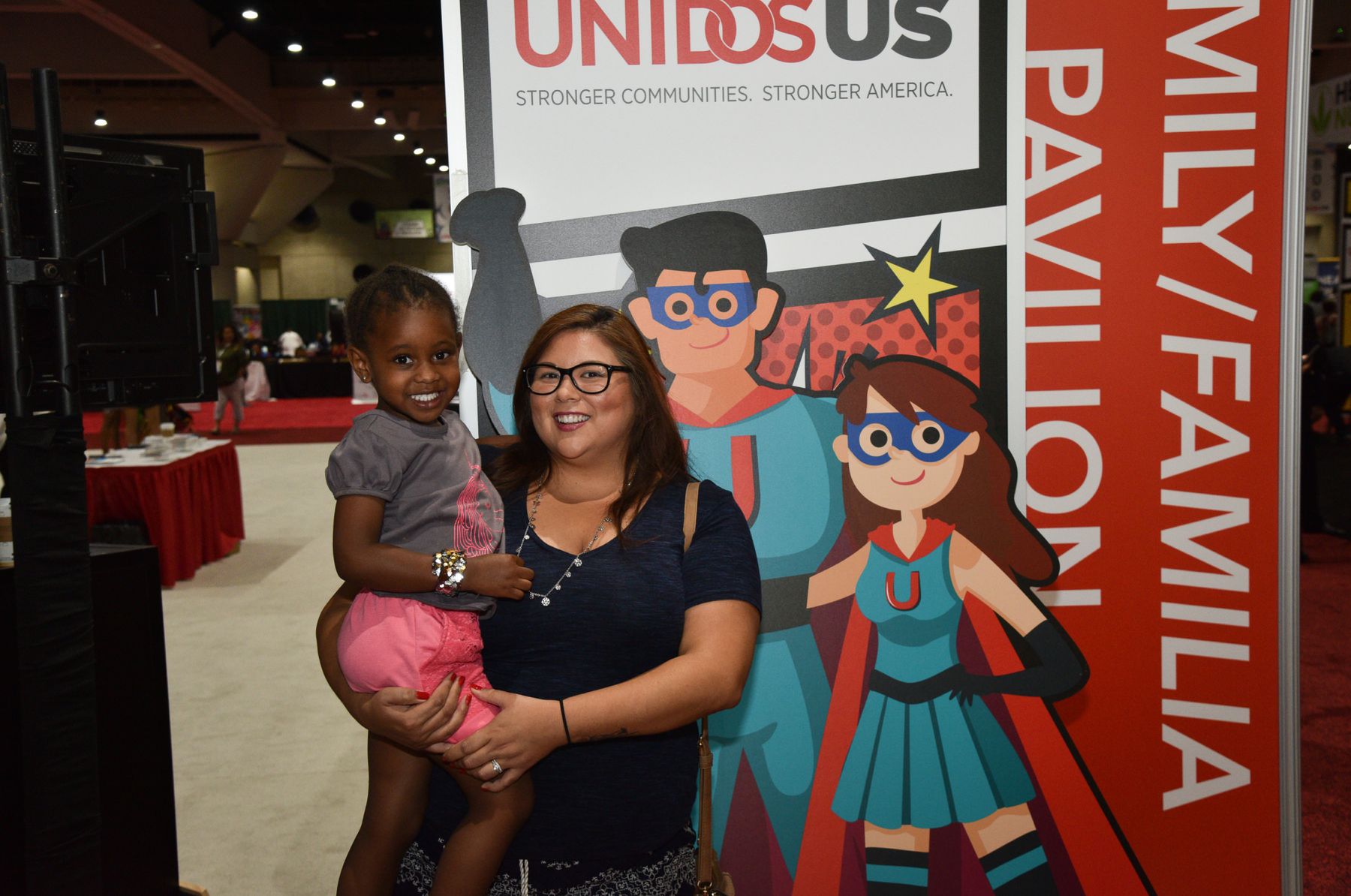 Mother and child in front of a UnidosUS sign that has two superhero characters.