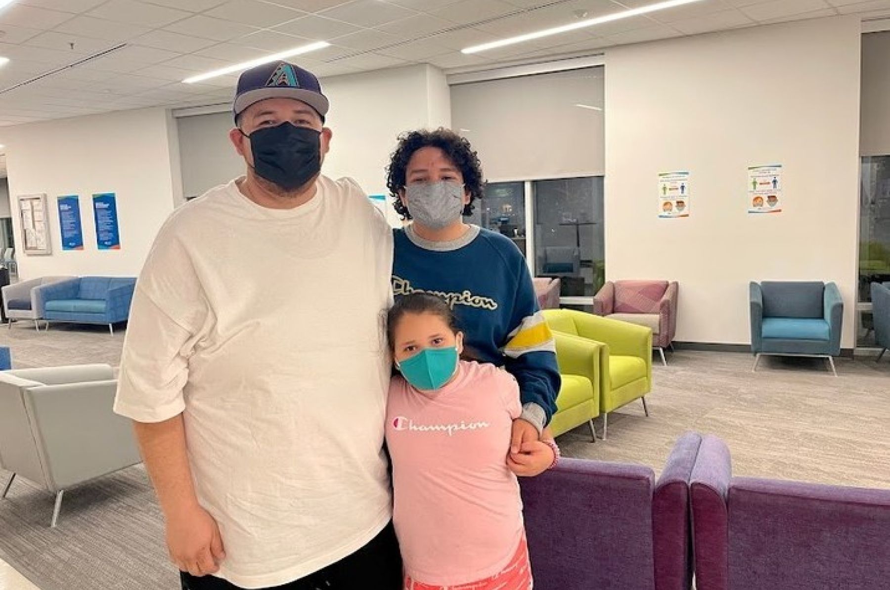 Masked family stands together inside a medical center waiting room.