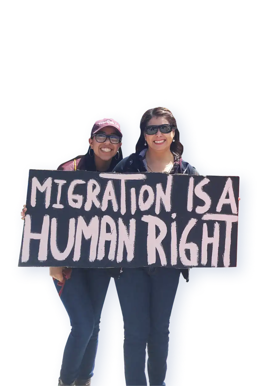 Two women at a march supporting immigration, holding a sign that states "Migration is a Human Right."