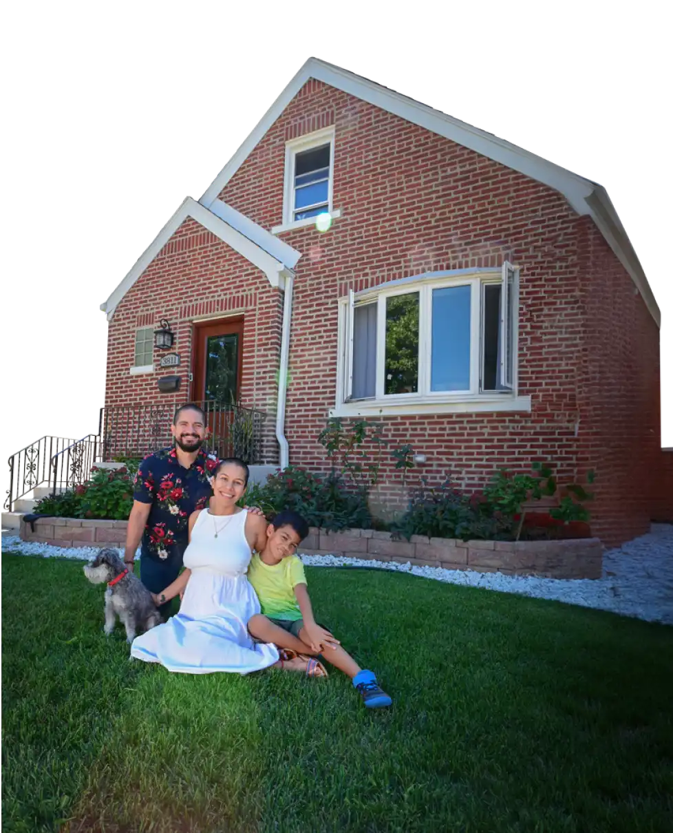 A young family of three, accompanied by their dog, sitting on the lawn outside their newly purchased home.